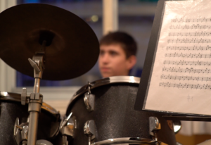 Primer plano de una batería y en el fondo un joven practicando en el Estudio Samela de Educación Musical (ESSEM)